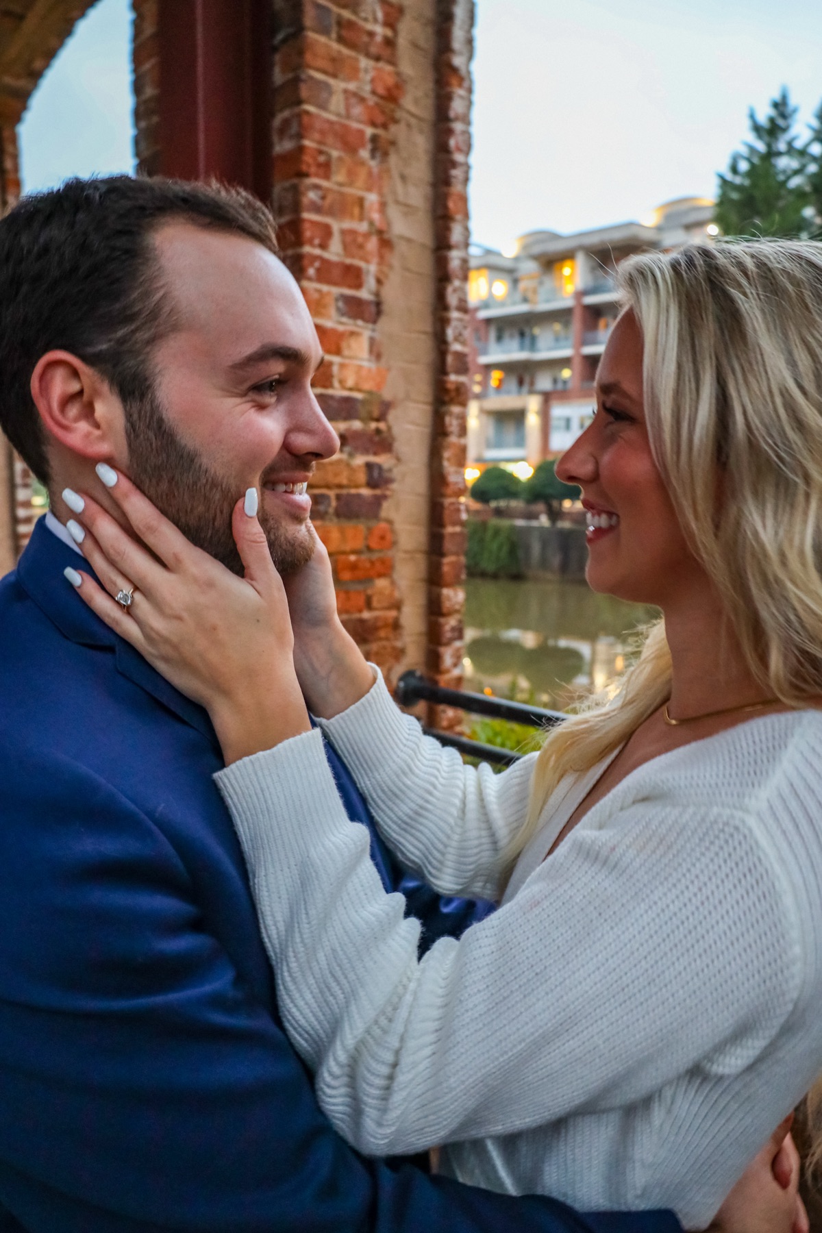 She holds his face, both of them laughing, by the river at RiverPlace