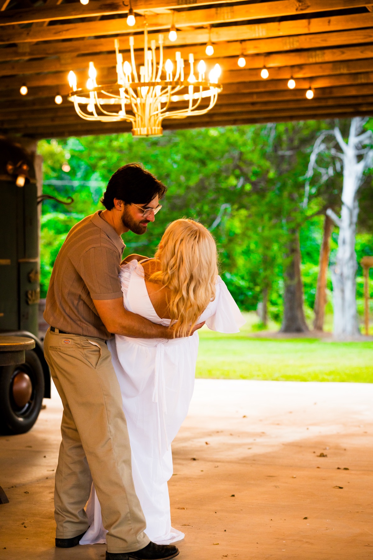 A couple under a chandelier hung in an open barn